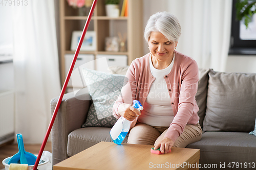 Image of senior woman with detergent cleaning table at home