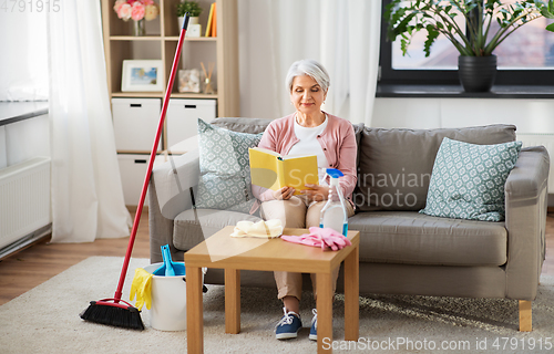 Image of senior woman reading book after home cleaning