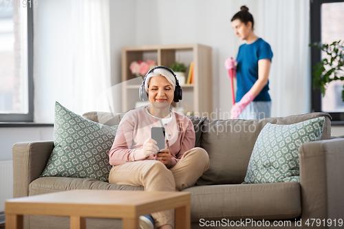 Image of old woman in headphones with smartphone at home