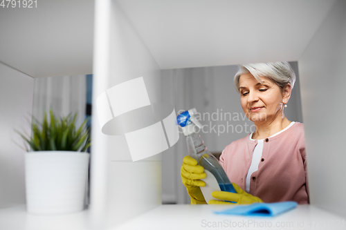 Image of senior woman cleaning rack with detergent at home