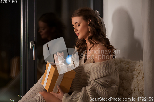 Image of woman with gift box at home at night
