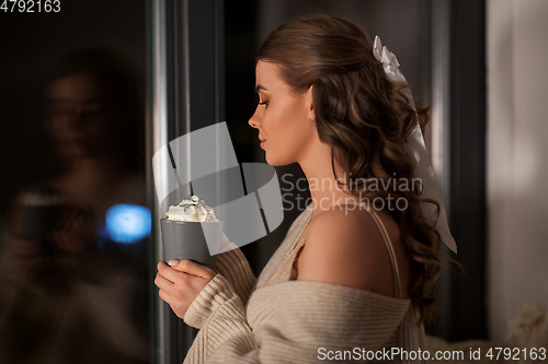 Image of woman holding mug with whipped cream at night