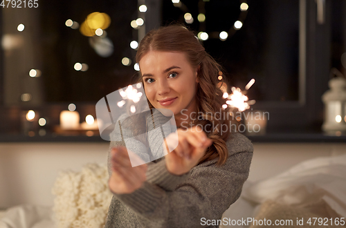 Image of happy young woman with sparklers in bed at home