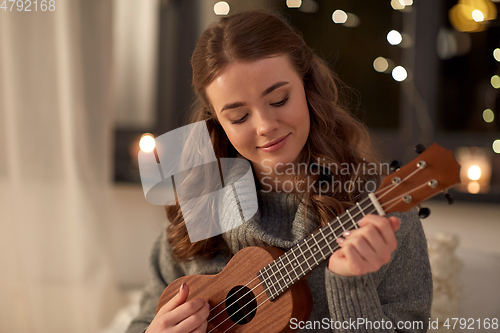 Image of happy young woman playing ukulele guitar at home