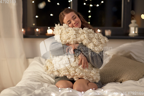 Image of happy young woman with soft pillow in bed at home
