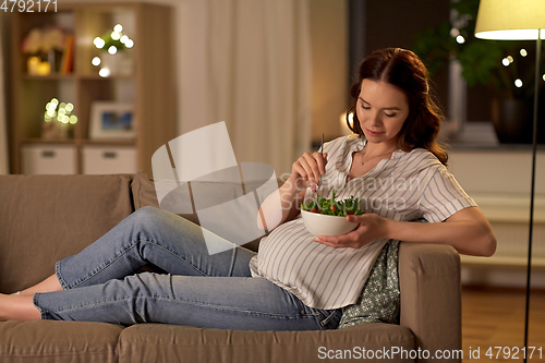 Image of happy smiling pregnant woman eating salad at home