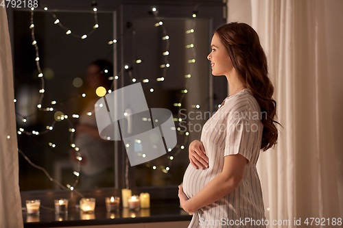 Image of happy pregnant woman looking out window at home