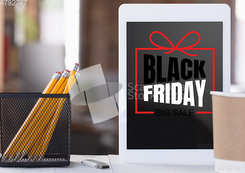 Image of Front view of tablet and office accessories with black friday lettering on blurred background