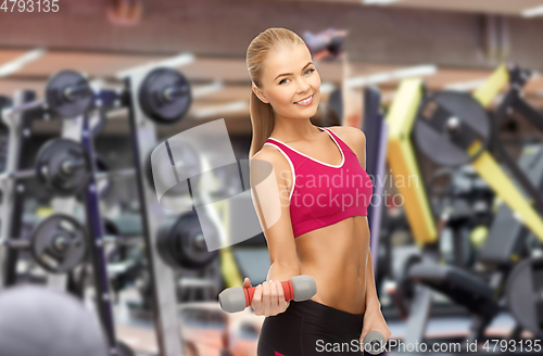 Image of happy young woman with dumbbells exercising in gym