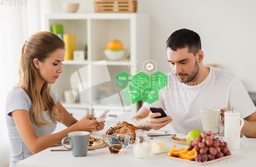 Image of couple with smartphones having breakfast at home