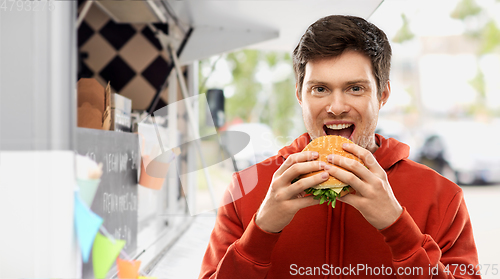 Image of happy young man eating hamburger at food truck