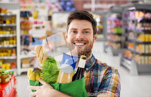 Image of smiling young man with food in bag at supermarket