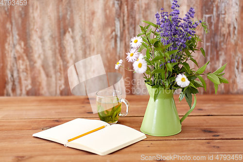 Image of herbal tea, notebook and flowers in jug on table