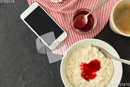 Image of porridge with jam, spoon, coffee and phone