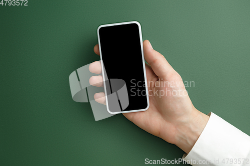 Image of Male hand holding smartphone with empty screen on green background for text or design