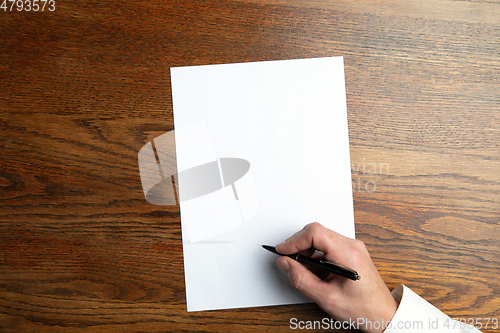 Image of Male hand holding pen and writing on empty sheet on wooden background for text or design