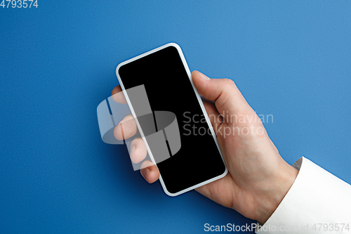 Image of Male hand holding smartphone with empty screen on blue background for text or design