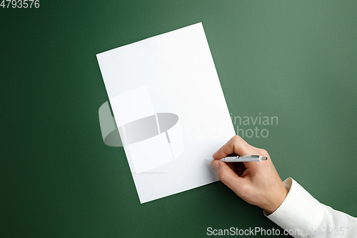 Image of Male hand holding pen and writing on empty sheet on green background for text or design