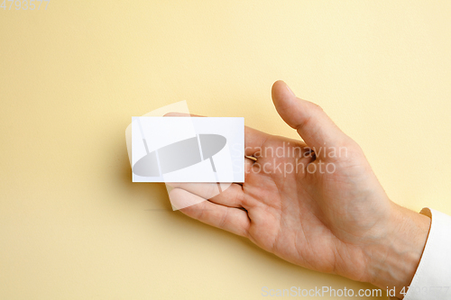 Image of Male hand holding a blank business card on soft yellow background for text or design