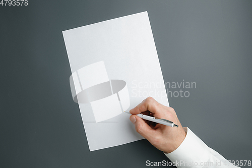 Image of Male hand holding pen and writing on empty sheet on grey background for text or design