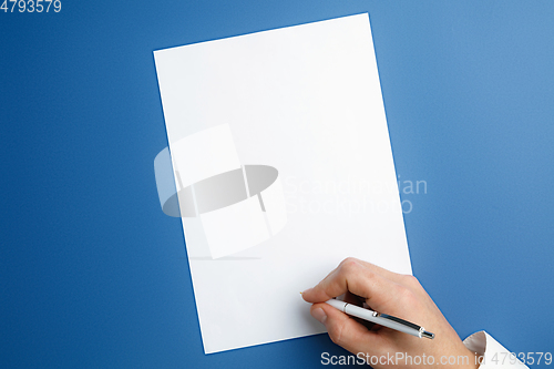 Image of Male hand holding pen and writing on empty sheet on blue background for text or design