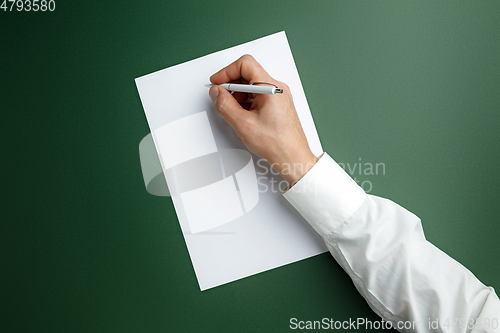 Image of Male hand holding pen and writing on empty sheet on green background for text or design