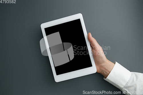 Image of Male hand holding tablet with empty screen on grey background for text or design