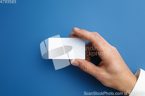 Image of Male hand holding a blank business card on blue background for text or design