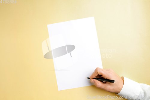 Image of Male hand holding pen and writing on empty sheet on yellow background for text or design