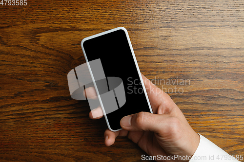 Image of Male hand holding smartphone with empty screen on wooden background for text or design