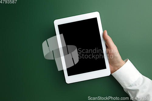 Image of Male hand holding tablet with empty screen on green background for text or design