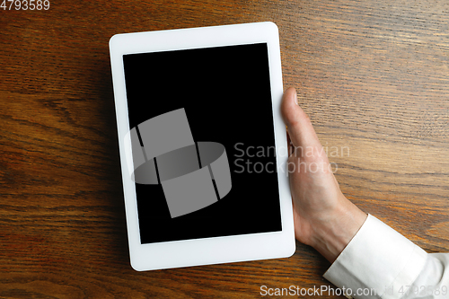 Image of Male hand holding tablet with empty screen on wooden background for text or design