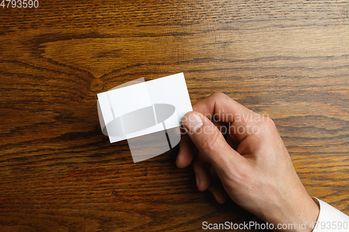 Image of Male hand holding a blank business card on wooden background for text or design