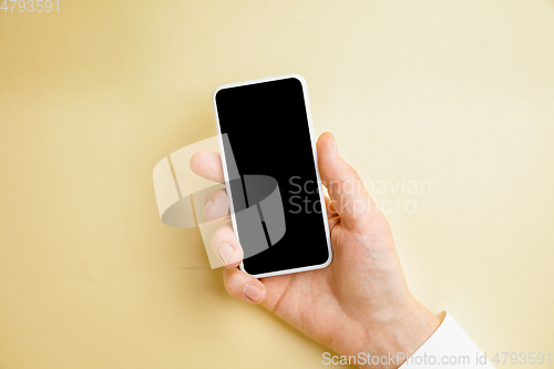 Image of Male hand holding smartphone with empty screen on yellow background for text or design