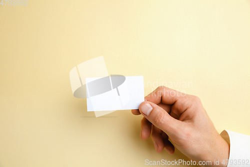 Image of Male hand holding a blank business card on soft yellow background for text or design