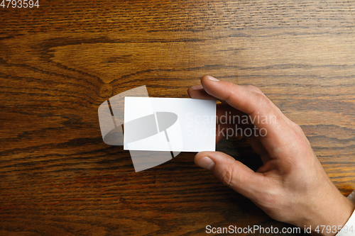 Image of Male hand holding a blank business card on wooden background for text or design