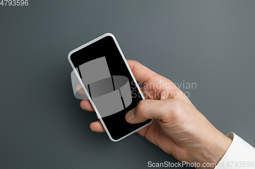 Image of Male hand holding smartphone with empty screen on grey background for text or design