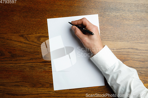 Image of Male hand holding pen and writing on empty sheet on wooden background for text or design