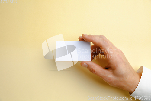 Image of Male hand holding a blank business card on soft yellow background for text or design