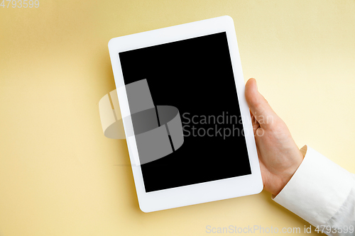 Image of Male hand holding tablet with empty screen on yellow background for text or design