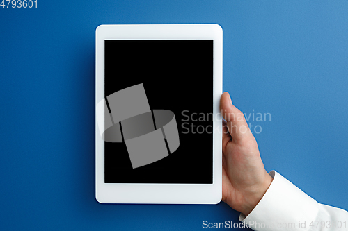 Image of Male hand holding tablet with empty screen on blue background for text or design