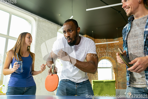 Image of Young people playing table tennis in workplace, having fun