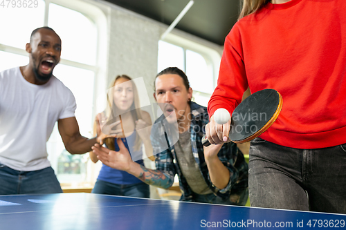 Image of Young people playing table tennis in workplace, having fun