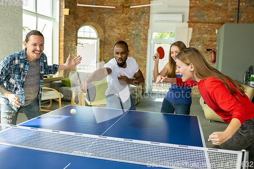 Image of Young people playing table tennis in workplace, having fun