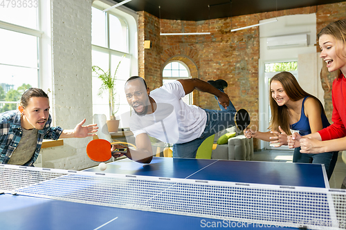 Image of Young people playing table tennis in workplace, having fun