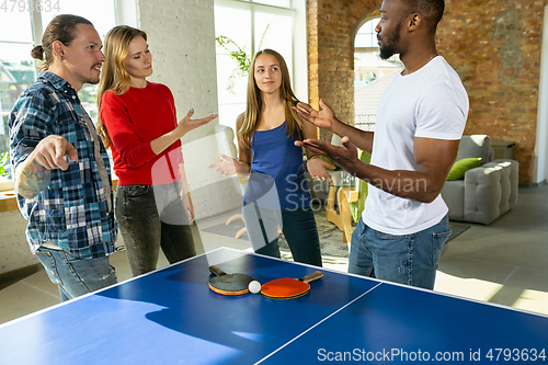 Image of Young people playing table tennis in workplace, having fun