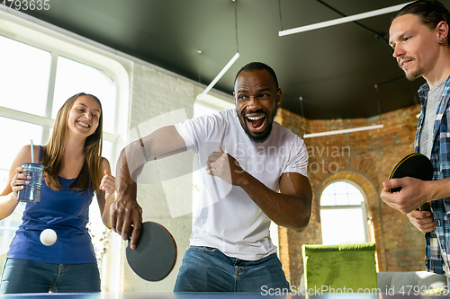 Image of Young people playing table tennis in workplace, having fun