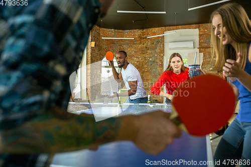 Image of Young people playing table tennis in workplace, having fun