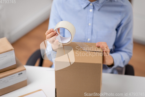 Image of woman packing parcel box with adhesive tape