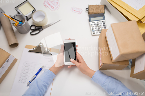 Image of hands with smartphone and parcels at post office